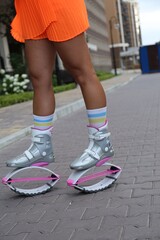 Fototapeta na wymiar Sporty woman doing exercises in kangoo jumping boots outdoors, closeup