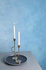 Holders with burning candles on grey table near light blue wall