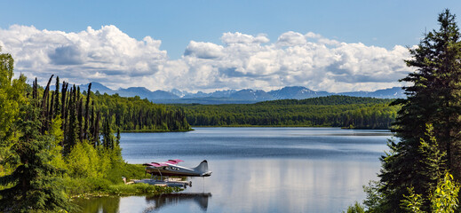 Obraz premium Floatplane docked on a peaceful, secluded lake with partial cloudy blue sky 