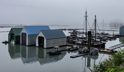 Small foggy marina with boat houses and an eerie mist background. 