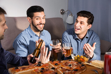 Friendly happy meeting in men company over beer with pizza at home