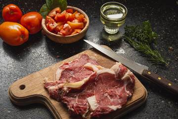 carne sobre tabla acompañado de ensalada de tomate, aceite, romero y perejil 