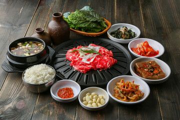 Bulgogi, a traditional Korean food on a black stone plate with a wooden background, and side dishes 나무배경에 검은 돌판위에 있는 한국 전통 음식인 불고기와 밑반찬
