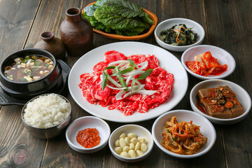 Bulgogi, a traditional Korean food on a black stone plate with a wooden background, and side dishes 나무배경에 검은 돌판위에 있는 한국 전통 음식인 불고기와 밑반찬