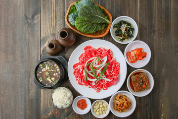 Bulgogi, a traditional Korean food on a black stone plate with a wooden background, and side dishes 나무배경에 검은 돌판위에 있는 한국 전통 음식인 불고기와 밑반찬