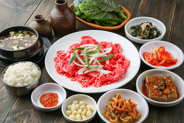 Bulgogi, a traditional Korean food on a black stone plate with a wooden background, and side dishes 나무배경에 검은 돌판위에 있는 한국 전통 음식인 불고기와 밑반찬