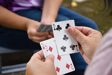 Paper cards number 5 holding in hands of woman who sitting and playing card with friend, soft and selective focus, freetimes and hobby activity at home concept.