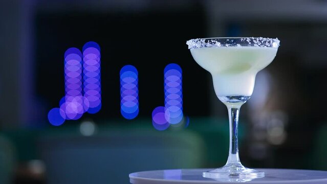 Glass goblet on the little rotating table. Light beverage with a piece of lime inside. Close up. Blurred backdrop.
