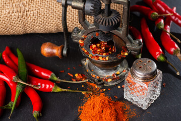 vintage mill and red hot peppers, pepper pods on a black table. Burlap bag. rustic style.