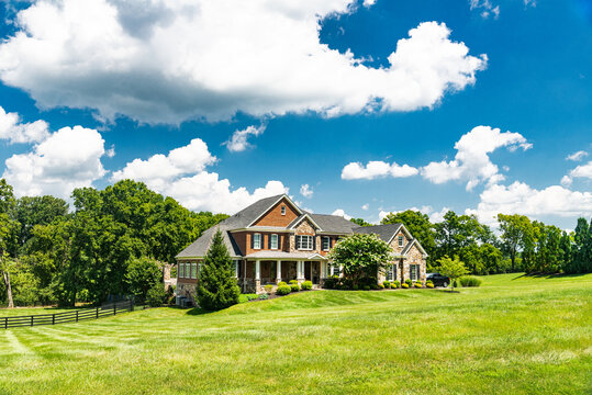 Large country white house and summer landscape with a perfect lawn. Blue sky and white clouds.