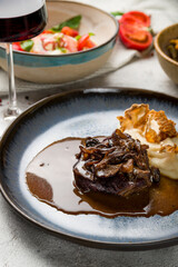Beef cheeks with mashed potatoes and mushrooms on demiglass sauce and red wine on glass on grey table