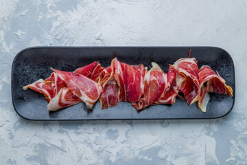 Spanish Jamon (Hamon), parma ham sliced on plate on white concrete table top view