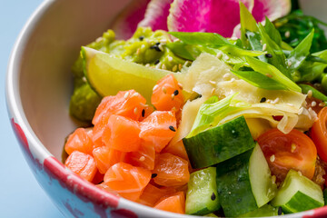 Poke with salmon, rice, cucumbers,tomatoes,edamame,avocado, ginger and chukka on plate macro close up on blue background