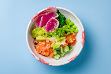 Poke with salmon, rice, cucumbers,tomatoes,edamame,avocado, ginger and chukka on plate top view on blue background