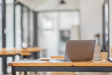 Laptop Computer, notebook, and eyeglasses sitting on a desk in a large open plan office space after working hours	
