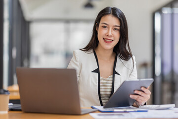 Female Business Asian working on documents on tablet laptop in the workplace, Young asian woman sitting at table doing planning financial report, business plan investment, finance analysis concept.