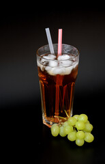 Grape juice with ice and straws in a tall glass on a black background.