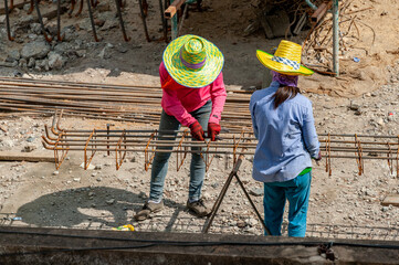Two construction workers equally spread out closed-loop steel bars along the length of deformed...