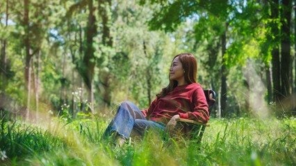Naklejka na ściany i meble Portrait image of a beautiful young asian woman sitting and relaxing on a chair in the park