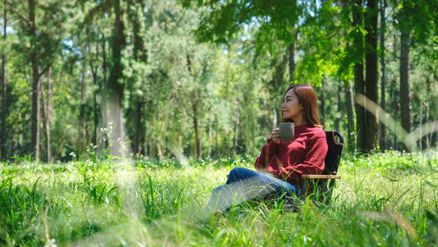 Portrait image of a beautiful young asian woman drinking coffee while sitting on a chair in the park