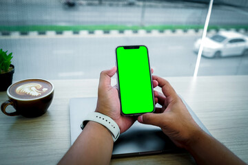 Mockup image of a business people holding smart mobile phone with blank green screen on vintage wooden table in modern cafe restaurant during meeting or lunch.