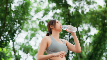 Young asian woman drinking water from a bottle while taking a break during her workout. Happy...