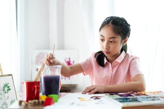 Little asian girl artist drawing on canvas with color palette and watercolor paint at home
