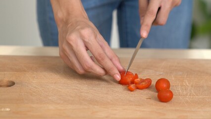Close up hands holding a knife preparing a contented meal. Sliced tomatoes and other vegetables on...
