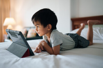 Asian little boy looking the screen of tablet on the bed in dark room, concept of kid and...