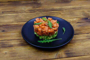 Salmon tartare with avocado and arugula on wooden table