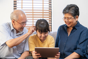 Happy family asian aged grandfather, grandmother have fun, smiling parent, girl using touchpad watching funny video call, play games and take photo selfie enjoy weekend together in living room at home