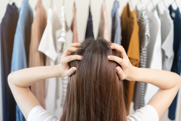Naklejka premium Choice of clothes, Nothing to wear. Attractive asian young woman try on appare, stressed choosing dress, outfit on hanger in wardrobe in room closet at home. Deciding blouse what to put on which one.