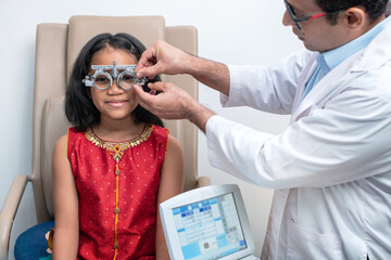Optometrist uses an trial frame to examine the vision of a little Indian child girl at an ophthalmology clinic, Vision devices for checking vision