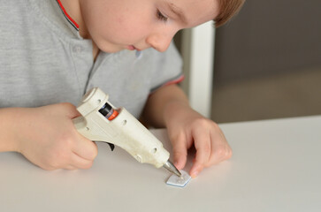 child glues a craft with a glue gun