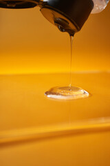 A drop of body gel or shampoo pouring from above on a yellow saturated background.