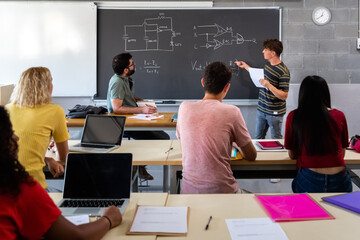 Teen male high school student giving oral class presentation in front of multiracial classmates....