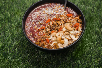 Antioxidant berry smoothie bowl on green grass, topped with seeds and nuts