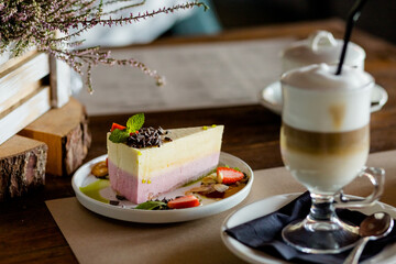 A piece of cheesecake and one glass of iced coffee.Glass of latte coffee and piece of lemon strawberry cheesecake on wooden table.Take a break with a Dessert