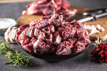 Fresh beef shank cuts piled in a bowl on a dark surface with herbs and spices around