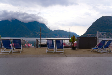 Fototapeta na wymiar Relax chairs at lakeshore at City of Lugano on a cloudy summer day. Photo taken July 4th, 2022, Lugano, Switzerland.