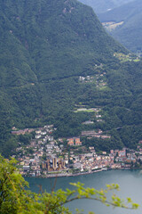 Fototapeta na wymiar Aerial view of mountains and lake with Italian Village of Campione seen from local mountain San Salvatore at City of Lugano on a cloudy summer day. Photo taken July 4th, 2022, Lugano, Switzerland.