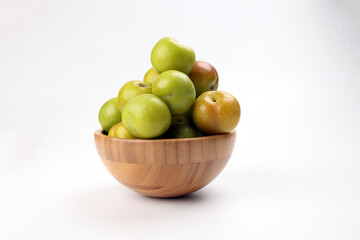 Small mini green fresh juicy plum fruit in wooden bowl on white background cut slice half