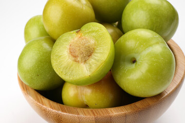 Small mini green fresh juicy plum fruit in wooden bowl on white background cut slice half