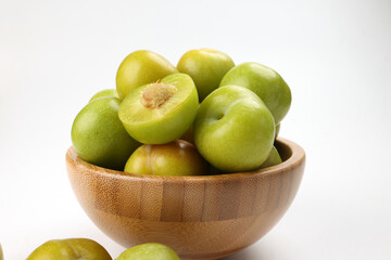 Small mini green fresh juicy plum fruit in wooden bowl on white background cut slice half