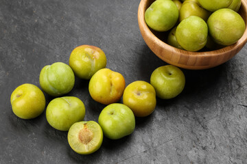 Small mini green fresh juicy plum fruit in wooden bowl on black slate stone board wooden table cut slice half seed