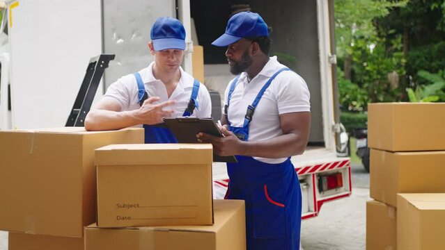 Workers unloading boxes from van outdoors.House move, mover service and Moving service concept.Two young handsome smiling workers wearing uniforms are unloading the van full of boxes.