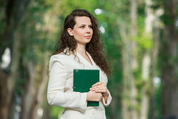 Fototapeta premium The portrait of a business woman with a notebook in her hand. Smartly dressed girl outside. Successful white european woman