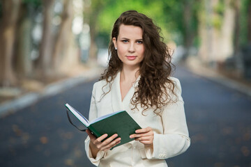 Obraz premium The portrait of a business woman with a notebook in her hand. Smartly dressed girl outside. Successful white european woman