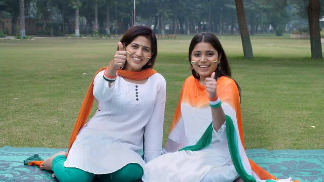 Two young Indian girls dressed in Indian tri colors chatting and posing for camera - thumbs-up  Republic Day. A young mother and her teenage daughter sitting together with National Flag tattoo on t...