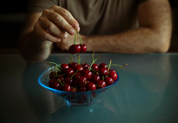 Hand of adult man holding cherries above bowl of cherries